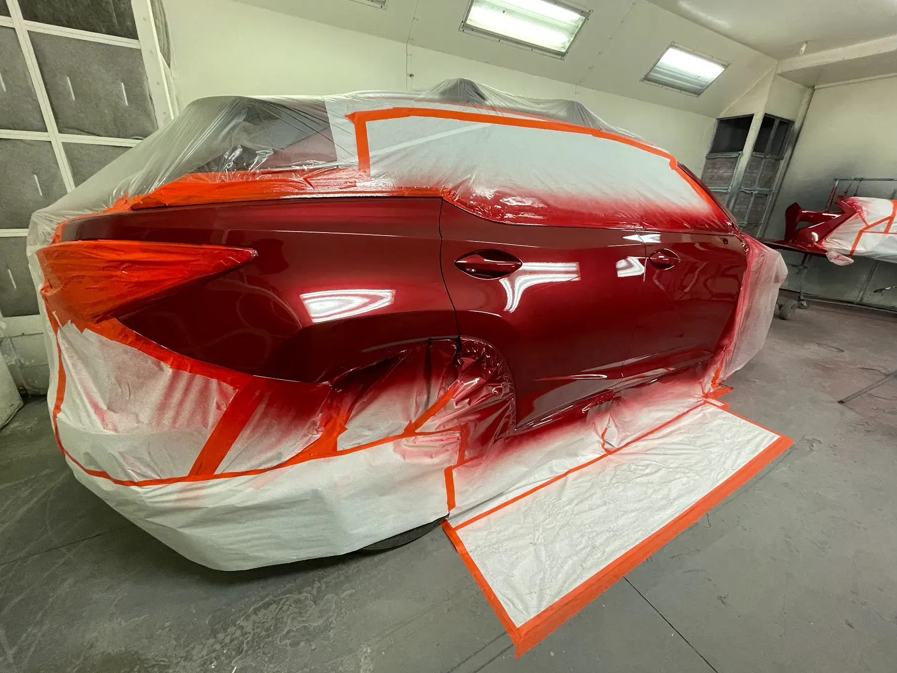 A newly painted car, showcasing precision work with protective coverings on areas to avoid unintended paint application, emphasizing attention to detail.