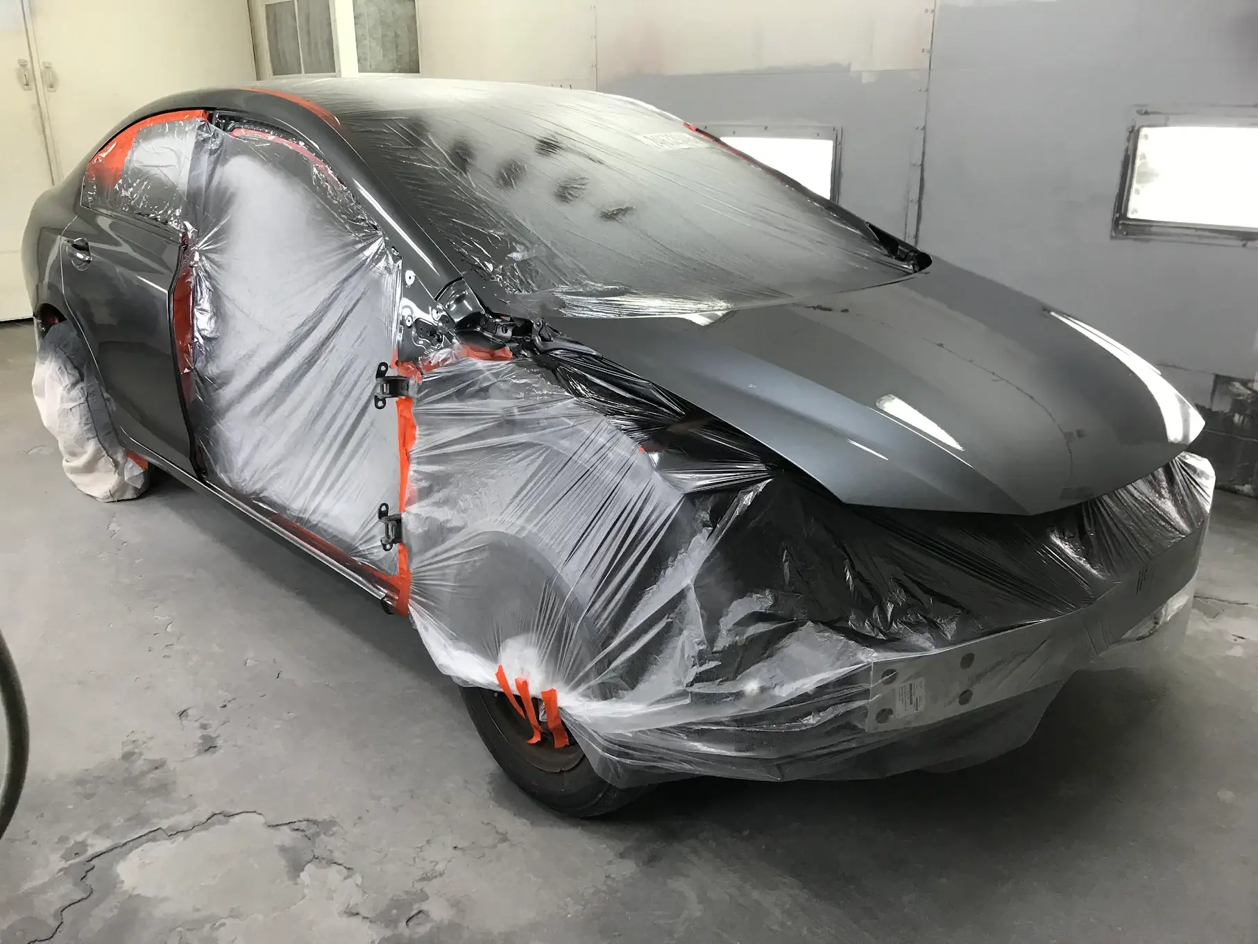 A newly painted car, showcasing precision work with protective coverings on areas to avoid unintended paint application, emphasizing attention to detail.