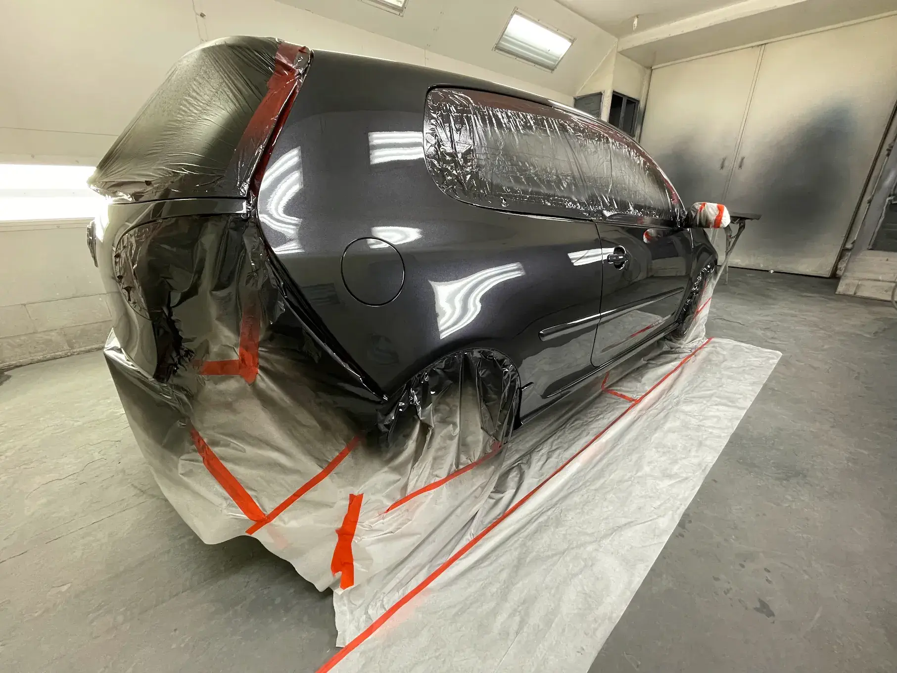 A newly painted car, showcasing precision work with protective coverings on areas to avoid unintended paint application, emphasizing attention to detail.