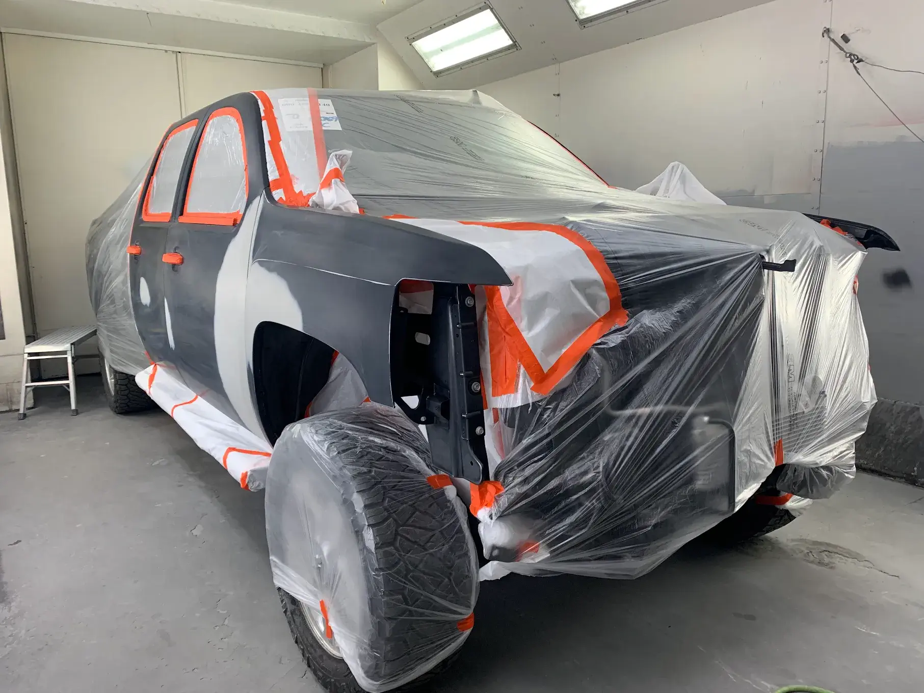 A newly painted car, showcasing precision work with protective coverings on areas to avoid unintended paint application, emphasizing attention to detail.