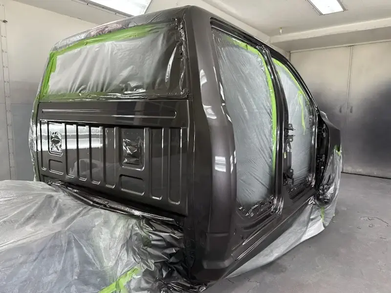 A newly painted car, showcasing precision work with protective coverings on areas to avoid unintended paint application, emphasizing attention to detail.