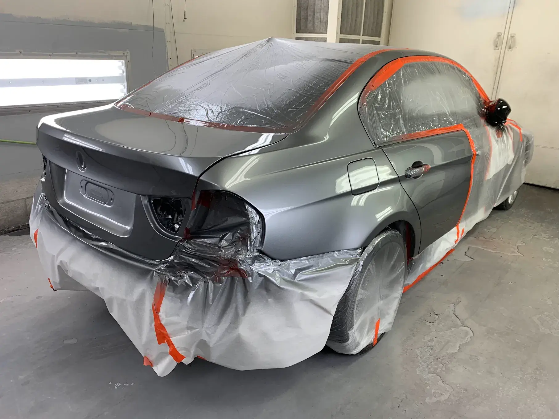 A newly painted car, showcasing precision work with protective coverings on areas to avoid unintended paint application, emphasizing attention to detail.