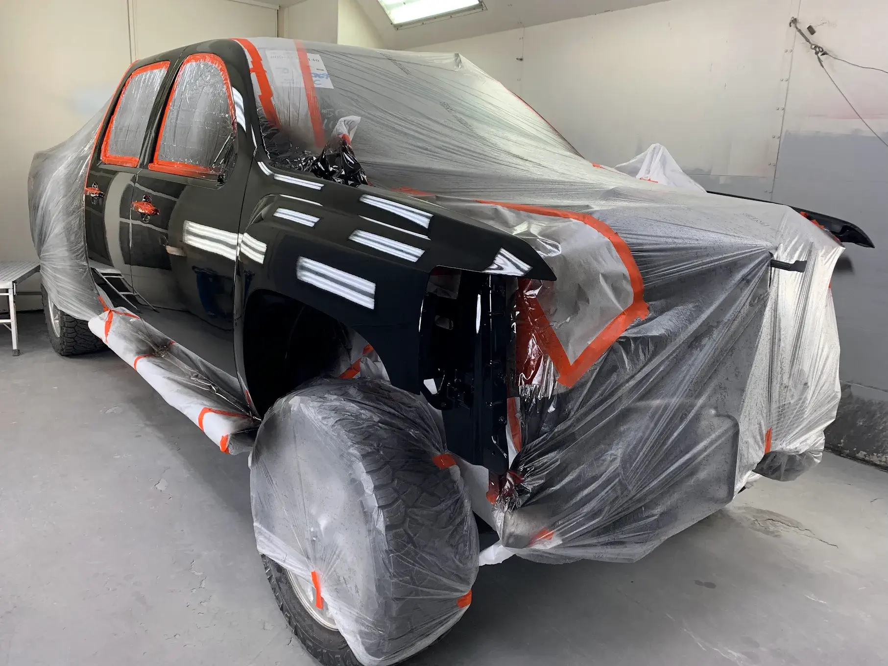 A newly painted car, showcasing precision work with protective coverings on areas to avoid unintended paint application, emphasizing attention to detail.