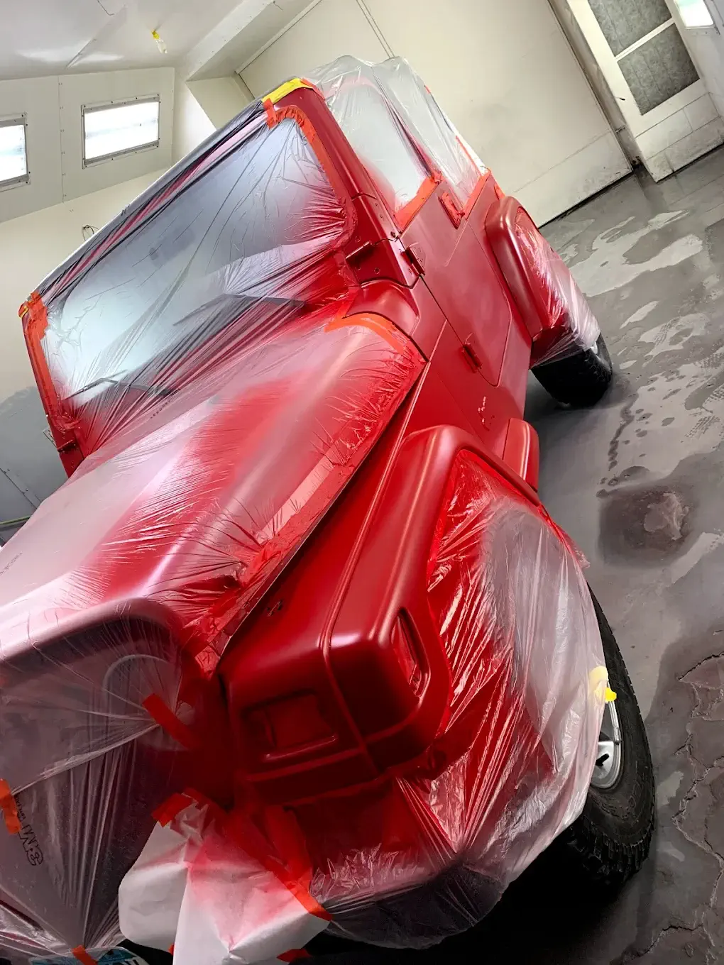 A newly painted car, showcasing precision work with protective coverings on areas to avoid unintended paint application, emphasizing attention to detail.