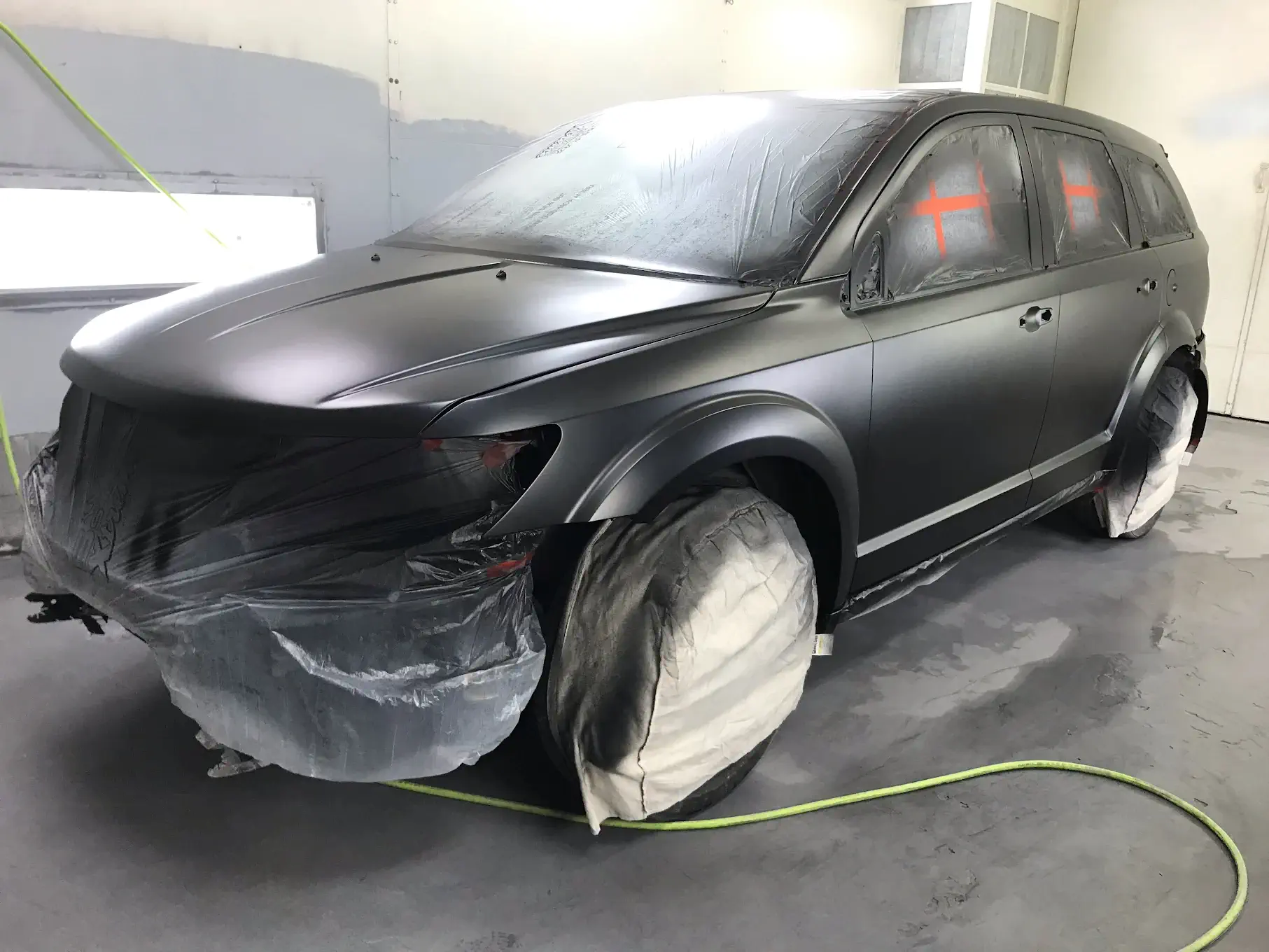 A newly painted car, showcasing precision work with protective coverings on areas to avoid unintended paint application, emphasizing attention to detail.