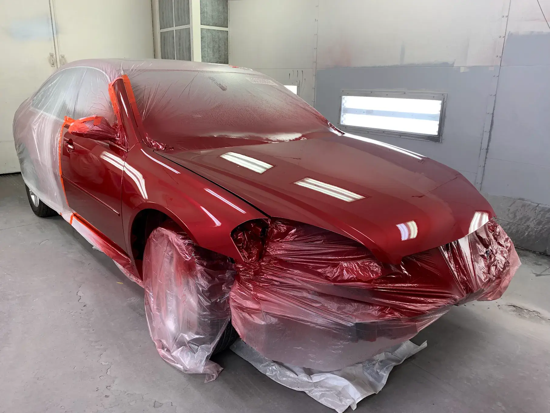 A newly painted car, showcasing precision work with protective coverings on areas to avoid unintended paint application, emphasizing attention to detail.