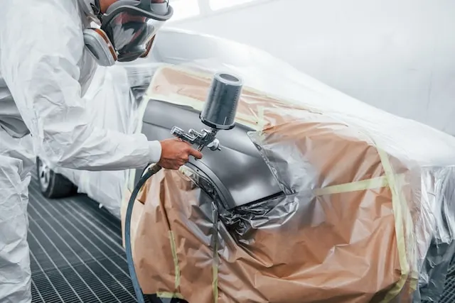 An automobile repairman in uniform works on a painting job in a garage, capturing the skilled craftsmanship and dedication in the automotive repair industry.