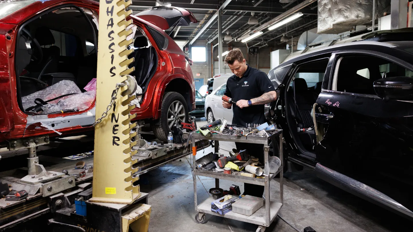 Technician repairing a damaged red car on a frame rack with chassis gauge visible
