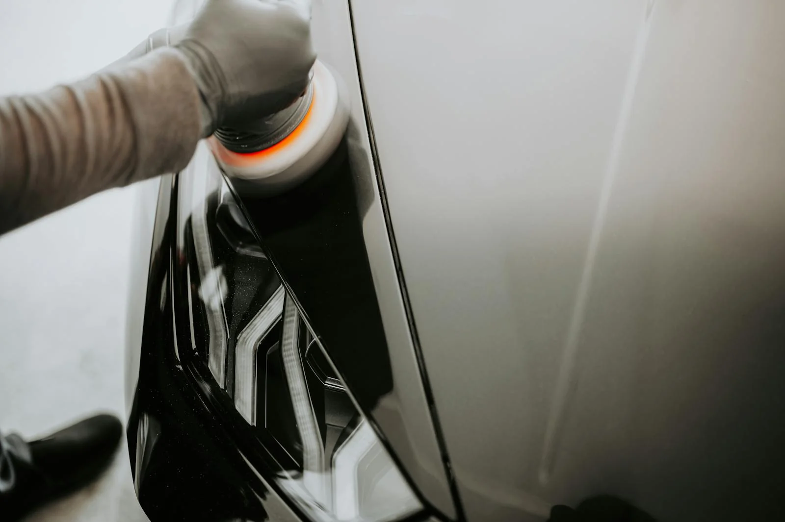 Gloved hand using an orange polishing pad to restore a yellowed car headlight